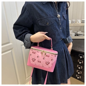 Close-up of pink bucket bag with cherry print held by model in casual setting