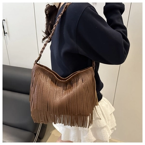 Détail d'un sac bandoulière en cuir marron avec franges et bandoulière tressée sur modèle