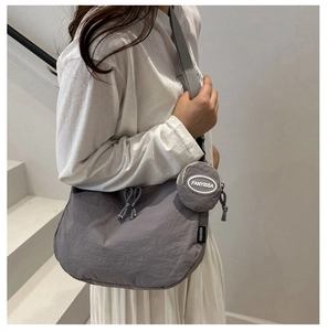Close-up of gray crossbody tote bag with mini round pouch shown on model in stairwell