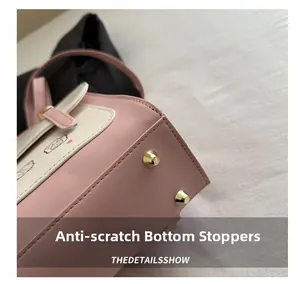 Detail of pink and beige handbag bottom featuring protective metal studs and stitching