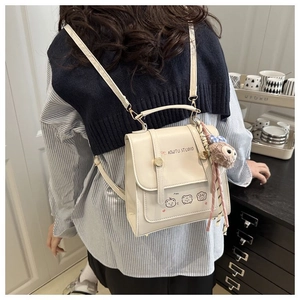 Detail of cream backpack with cartoon bear prints and a plush brown charm accessory
