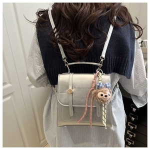 Close-up of metallic silver backpack featuring a polished handle and a cute plush bear charm
