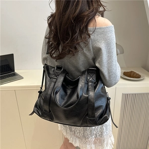 Black large capacity soft leather tote bag worn by a model in a casual city setting