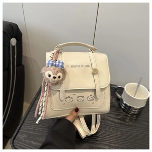 Close-up of cream white backpack with cartoon bears and plush pendant on table