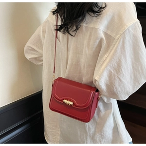 Side view of a vintage red square crossbody bag with gold metal buckle on a white shirt