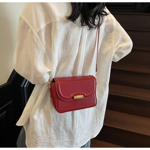 Detail of red leather crossbody bag with golden twist lock worn on white shirt