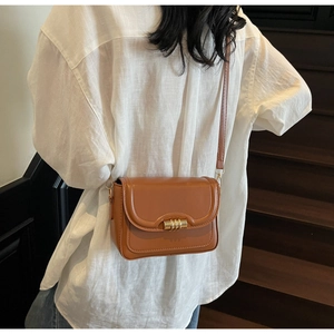 Detailed close-up of a brown leather shoulder bag featuring a gold metal buckle design