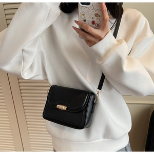 Classic black leather crossbody bag featuring a round gold twist lock shown on a white hoodie