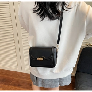 Detail of minimalist black crossbody bag with gold twist lock on casual outfit