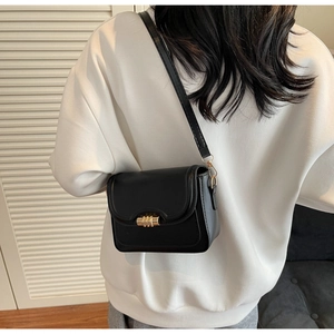Detail of a black leather crossbody bag with a gold metal clasp shown on a model