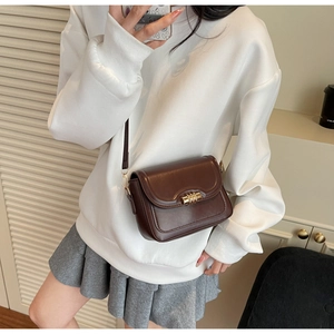 Detail view of brown leather crossbody bag with gold twist lock on a white sweater outfit