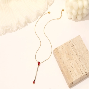 Collier élégant en or avec pendentif vertical en pierre rouge sur fond décoratif beige