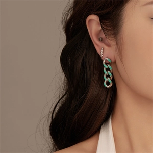 Close-up of dangling chain earrings with turquoise enamel on a model for piercing style