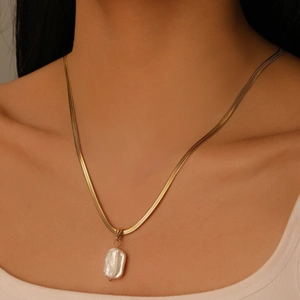 Detailed view of model wearing a gold snake chain necklace with baroque pearl pendant