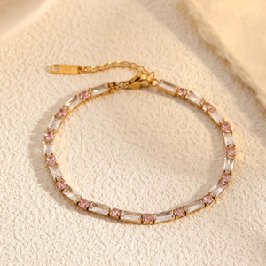 Golden bracelet with alternating rectangular clear and round pink zircons on textured background