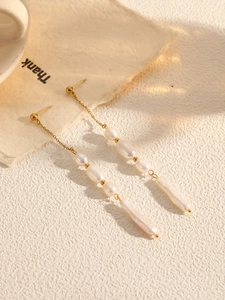 Detailed close-up of long tassel earrings with baroque pearls and golden chain links
