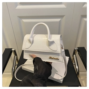 Detail of white crocodile pattern leather handbag with gold logo and elegant handle