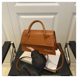 Detail of caramel brown croc-embossed trapezoid handbag with gold logo and top handle