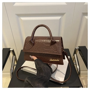 Detail view of deep brown crocodile embossed leather handbag with gold metal logo finish