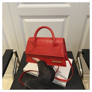 Detail of red crocodile embossed leather handbag with gold logo and shoulder strap