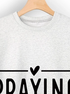 Détail du col d'un sweat-shirt gris et graphique cœur avec texte Praying sur tissu