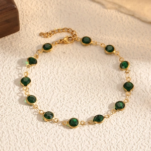 Dettaglio del bracciale a catena dorata con gemme verde scuro, chiusura a moschettone