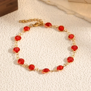 Dettaglio del bracciale a catena dorata con pietre rosse e chiusura a moschettone su pietra