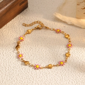 Détail du bracelet doré avec marguerites roses et breloques cœur sur une surface texturée