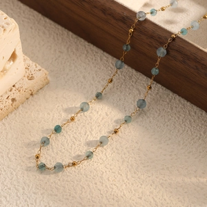 Elegant layered necklace with aquamarine blue beads and gold chain on wooden tray