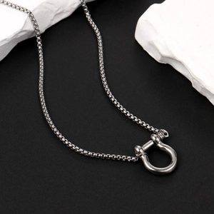 Close-up of a silver horseshoe shackle pendant on a sleek steel box chain over stone