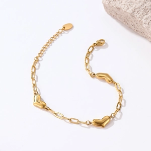 Minimalist gold paperclip chain bracelet featuring polished heart charms on white background