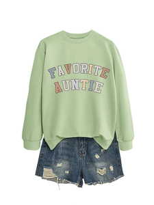 Dettaglio della felpa verde chiaro con scritta Favorite Auntie e shorts in denim usurati