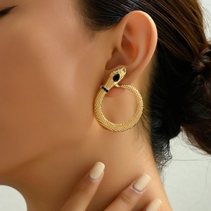 Golden snake hoop earrings with scale texture and black stones on elegant female model