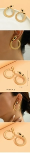 Detailed close-up of golden snake hoop earrings with scale texture and black drop accents