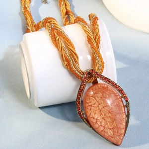 Détail d'un collier bohème orange perlé avec pendentif goutte d'eau sur une tasse blanche