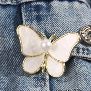 Elegante spilla a farfalla dorata con ali in madreperla e perla su sfondo in denim
