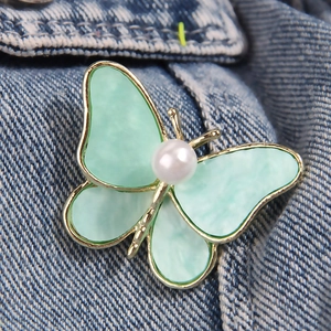Spilla a farfalla verde menta elegante con perla su sfondo in denim blu scuro