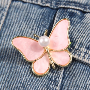 Spilla a farfalla dorata con ali in smalto rosa e perla su tessuto denim blu