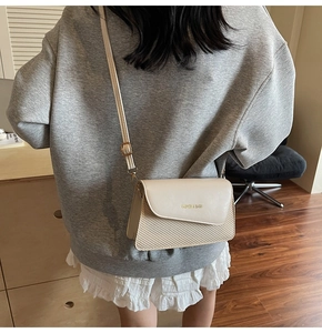 Model wearing a beige crossbody bag with woven texture and gold lettering detail