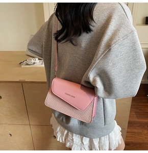 Detail of pink crossbody bag with wide strap showing woven texture and gold lettering
