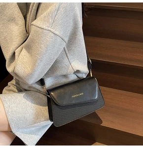 Detail of black crossbody bag with diagonal quilted texture and gold hardware on model