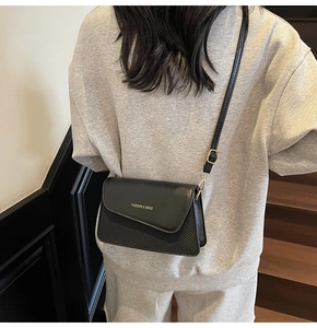 Detailed view of the black crossbody bag with gold lettering and mixed texture material