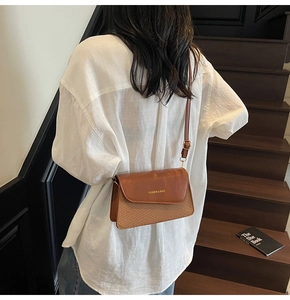Detail of a brown textured crossbody bag featuring leather and woven patchwork design