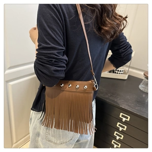 Detail of a brown fringe bucket bag with silver studs worn by a model in a cozy room