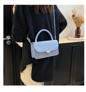 Detail of light blue crossbody bag featuring silver metallic buckle and textured leather