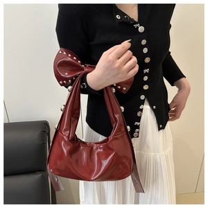Détail du sac à main rouge foncé avec un grand nœud clouté et une finition en cuir verni brillant