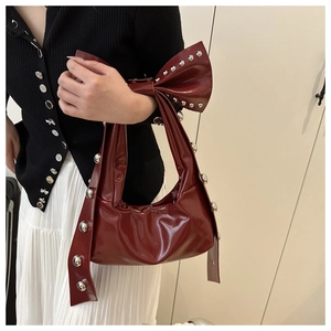 Detail of burgundy patent leather bag with large studded bow decoration and glossy finish