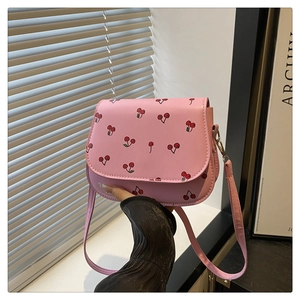 Detail of pink crossbody bag with red cherry pattern and golden metal hardware