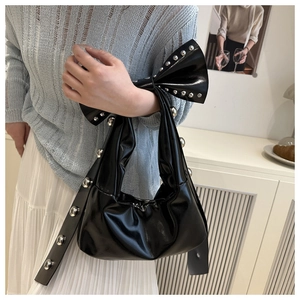 Detail of black glossy bow handbag with silver metal studs and studded shoulder strap