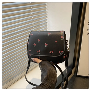 Detail of red cherry print on black PU leather handbag with silver metal buckle